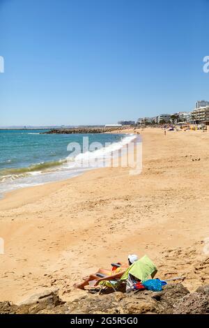 Quarteira, Portugal. 29 juin 2021. Une seule femme bronze sur une plage occupée par ailleurs au milieu de la pandémie de Corona. L'Institut Robert Koch a classé le pays comme une zone de variante de virus - et donc quelques touristes allemands commencent à la hâte leur voyage de retour. Toute personne revenant du Portugal en Allemagne doit passer 14 jours en quarantaine et ne peut pas être autorisée. Credit: Vasco Célio/dpa/Alay Live News Banque D'Images