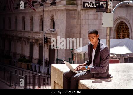 Un homme noir voyage, travaille à New York, assis dans une rue à côté d'un immeuble de bureaux d'époque, lit et travaille sur un ordinateur portable. Le W Banque D'Images