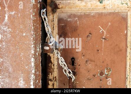 Ancienne porte abîmé d'une maison abandonnée verrouillée avec une chaîne et un cadenas rouillé. Banque D'Images