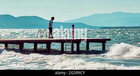 Urla, İzmir, Turquie - juin 2021 : un père parle à son fils sur un ponton en bois au-dessus de la mer à Urla, İzmir, Turquie.