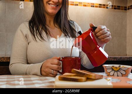 Gros plan d'une femme de Latina se versant un café au milieu d'un petit déjeuner maison. Banque D'Images