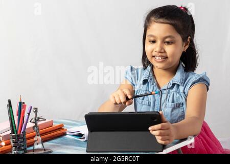 Une jolie petite fille indienne fréquentant un cours en ligne avec une tablette sur fond blanc Banque D'Images