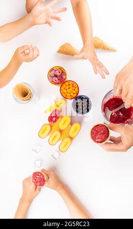 les enfants tiennent une cuillère de glace aux baies maison dans un cône de gaufres sur une table blanche. Dessert sain d'été nourriture végétarienne Banque D'Images