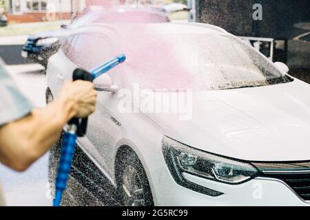 Lavage manuel de voiture avec de l'eau sous pression dans les lavages de voiture, une personne lave la mousse de la voiture avec de l'eau haute pression Banque D'Images