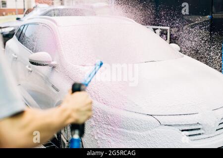 Lavage manuel de voiture avec de l'eau sous pression dans les lavages de voiture, une personne lave la mousse de la voiture avec de l'eau haute pression Banque D'Images