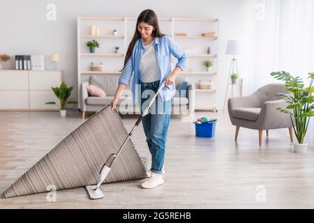 Portrait d'une femme qui nettoie le sol dans la salle de séjour à l'aide d'une vadrouille Banque D'Images
