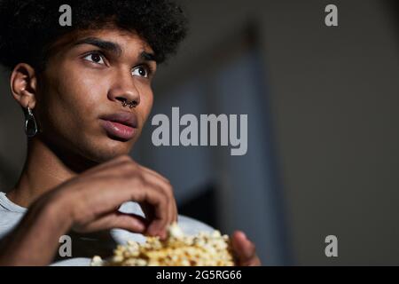 Gros plan d'un jeune homme qui prend du pop-corn dans un bol tout en regardant un film à la maison Banque D'Images