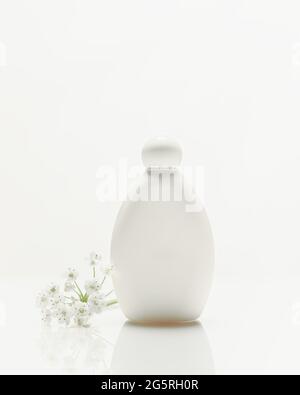 Composition cosmétique blanche verticale avec bouteille cosmétique en plastique avec reflet et fleurs sur fond blanc avec espace de copie. Produit de beauté Banque D'Images