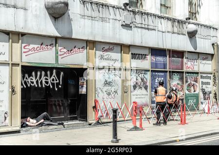 Manchester, Royaume-Uni. 29 juin 2021. Les nettoyeurs de fenêtres ignorent l'homme endormi sans abri dans la porte à côté d'eux.dans la Tour Beethan de l'ombre de Manchester, une tente est là pour rappeler sans ambages l'épidémie extrême de sans-abri de Manchester. Lors de sa campagne électorale de 2017, Andy Burnham a promis de débarrasser la ville des sans-abri, mais la pandémie a aggravé la situation. Crédit : SOPA Images Limited/Alamy Live News Banque D'Images