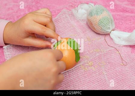 Le processus de teinture des œufs en pelures d'oignon. Coloration écologique des oeufs pour Pâques. Dessin de feuilles de persil. Main des enfants. Banque D'Images