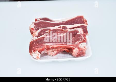 tranches d'agneau fraîchement hachées décorées dans un plat sur fond blanc, portion de longe Banque D'Images