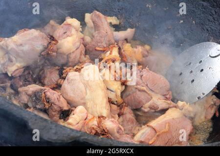 Gros morceaux de viande d'agneau avec dumba de graisse d'agneau frits en gros dans l'huile avec des bulles dans un chou-fleur noir, cuisine Banque D'Images