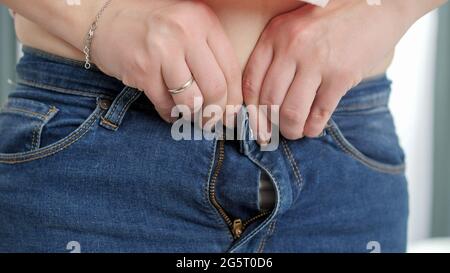 Femme grosse avec le gros ventre essayant de tirer et de bouton vers le haut jeans serrés. Concept de poids excessif, de femmes obèses, de régime et de problèmes de surpoids Banque D'Images