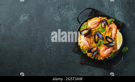 Paella traditionnelle espagnole de fruits de mer en casserole avec pois chiches, crevettes, moules, calmars sur fond de béton noir. Vue de dessus avec espace de copie Banque D'Images