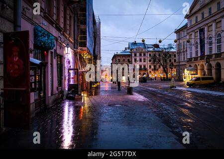 Lviv, Ukraine - 28 décembre 2019 : rue de la place du marché de la vieille ville à Lvov avec neige d'hiver le soir sombre avec route vide et réflexion Banque D'Images