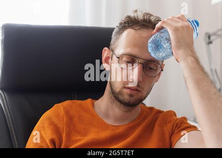 Un homme travaillant à la maison souffrant de chaleur et de soif se rafraîchit avec une bouteille d'eau à la chaude journée d'été Banque D'Images