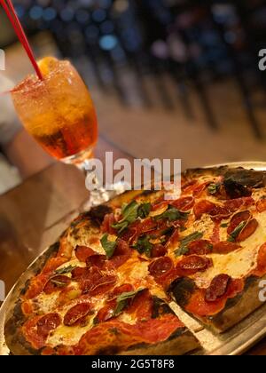Gros plan d'une pizza au pepperoni fraîchement cuite avec des feuilles de basilic servie avec un cocktail coloré sur une table en bois dans un cadre de restaurant Banque D'Images