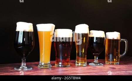 Six bières différentes dans six verres différents se tiennent dans une rangée sur une table en bois. Gros plan. Banque D'Images