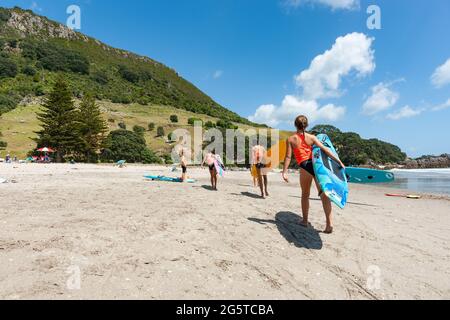 Mount maunganui Nouvelle-Zélande - janvier 20 2015 ; adolescents transportant des planches à aubes le long de la plage Banque D'Images