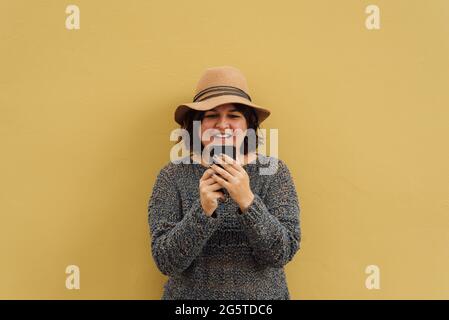 Portrait d'une femme moderne qui fait ses achats en ligne avec son mobile. Une fille utilisant son smartphone, chapeau appuyé sur un mur dans la rue. Copier l'espace Banque D'Images