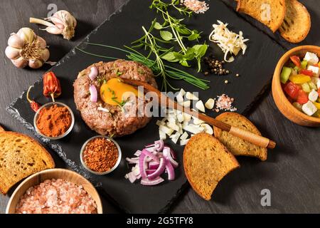 Steak tartre à l'oignon haché et aux herbes sur un panneau d'ardoise noire.steak traditionnel français maison tartare de bœuf cru. Banque D'Images