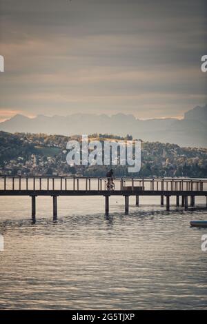 Un motard traversant un pont au-dessus d'un plan d'eau avec des montagnes en arrière-plan, Zurich, suisse Banque D'Images