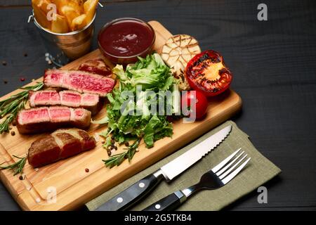 Steaks de bœuf rôtis grillés, pommes de terre et sauce sur planche à découper en bois Banque D'Images