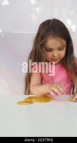 Enfant jouant à la main fait Toy appelé Slime. Jolie fille dans un t-shirt rose joue avec un slime jaune. Créativité contemporaine. Étirements, scamming, modelage Banque D'Images