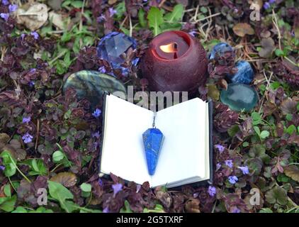Gros plan avec bougie brûlante, livre ouvert pour les sorts et les cristaux magiques dans l'herbe dehors. Arrière-plan ésotérique, gothique et occulte, Halloween mystique et W. Banque D'Images