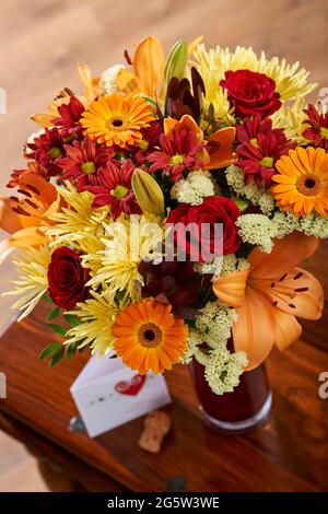 Bouquet de fleurs mélangées dans un vase en verre rouge sur une table basse Banque D'Images