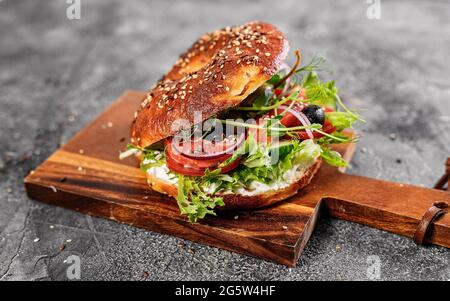 Bagel New-yorkais au fromage à la crème, salade, concombre, herbes, olives et poisson rouge salé. Salade sandwich maison sur planche à découper. Excellent délicieux Banque D'Images