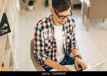 Un travailleur masculin attrayant utilise un ordinateur à la cafétéria, un jeune homme travaille à l'aide d'un ordinateur portable Banque D'Images