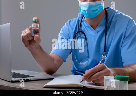 Un médecin de race blanche portant un masque facial contenant un flacon de vaccin Banque D'Images