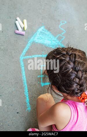 L'enfant dessine la maison avec de la craie sur l'asphalte. Focus sélectif. tirage. Banque D'Images