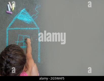 L'enfant dessine la maison avec de la craie sur l'asphalte. Focus sélectif. tirage. Banque D'Images