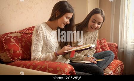 Deux écolières souriantes souriant souriant, assis sur un canapé et écrivant dans les journaux intimes Banque D'Images