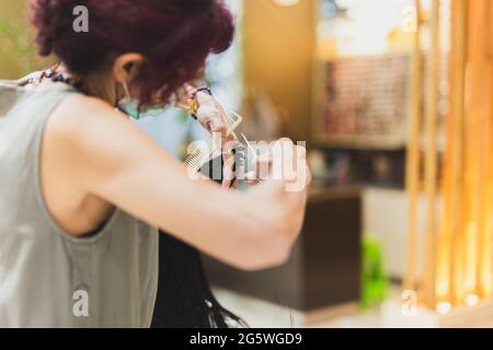 Coiffeur tient le peigne et les ciseaux dans ses mains et coupe les cheveux des clients. Banque D'Images