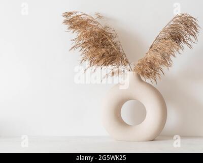 Sécher les branches de roseau d'automne dans un vase rond en céramique. Décoration intérieure minimaliste. Vue avant. Copier l'espace Banque D'Images