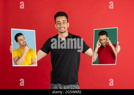 Jeune homme tenant ses portraits isolés sur fond rouge studio avec espace de copie pour la publicité. Banque D'Images