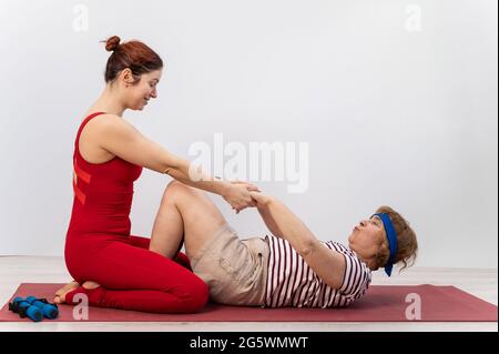 L'entraîneur aide la femme âgée à faire de la forme physique sur un fond blanc Banque D'Images