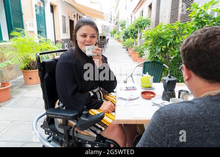 Bonne femme handicapée en fauteuil roulant, buvant du café avec un petit ami sur la terrasse du restaurant Banque D'Images