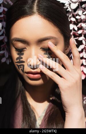 Femme japonaise avec hiéroglyphes touchant le visage isolé sur le noir Banque D'Images