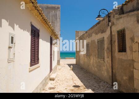 Sampieri, Ragusa, Sicile, Italie. Voie étroite entre les maisons de pêcheurs traditionnelles, les eaux turquoise de la mer Méditerranée au-delà. Banque D'Images