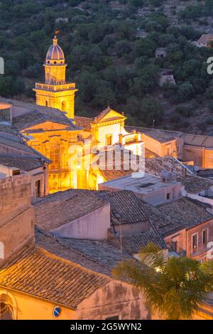 Ragusa, Sicile, Italie. Vue sur les toits carrelés au crépuscule, la façade et le clocher de l'église de Santa Maria dell'Itria sont illuminés. Banque D'Images