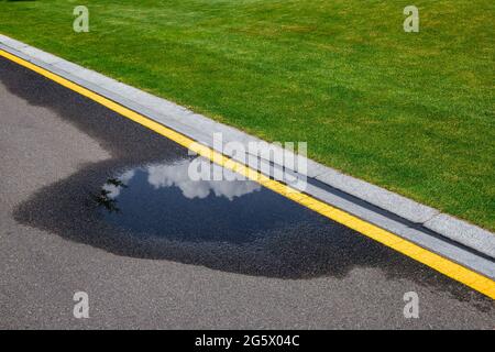 flaque sur la route asphaltée avec des eaux pluviales sur le côté de la route avec un fossé pour l'eau et une glade de pelouse verte le long de la route. Banque D'Images