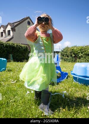 Jeune fille vêtue comme une fée regardant à travers des jumelles, Cornwall, Royaume-Uni Banque D'Images