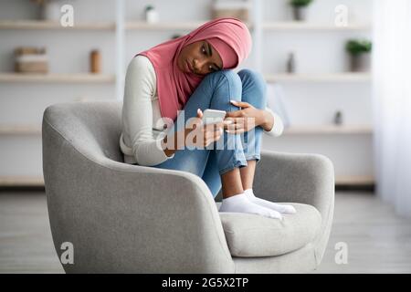 Contrarié la femme musulmane noire dans hijab lisant le message sur le smartphone à la maison Banque D'Images