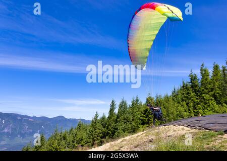 Femme aventureuse volant sur un parapente autour du paysage de montagne canadien Banque D'Images