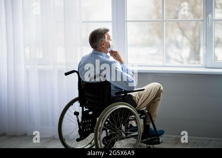 Un vieil homme handicapé en fauteuil roulant portant un masque facial, souffrant de solitude dans une maison de retraite pendant un covid Banque D'Images