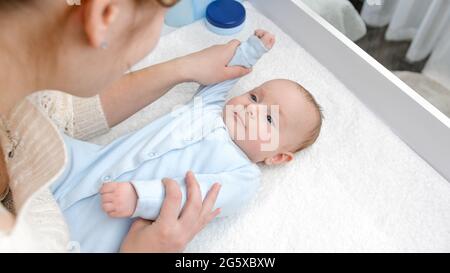 Un joli petit garçon souriant tandis que la mère fait de la gymnastique et des massages sur la coiffeuse. Concept d'hygiène, de soins de bébé et de soins de santé Banque D'Images